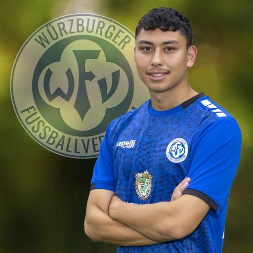 Fußballspieler vom Würzburger FV im blauen Trikot mit Vereinslogo im Hintergrund Fußballspieler im blauen Trikot vom Würzburger FV vor Vereinslogo