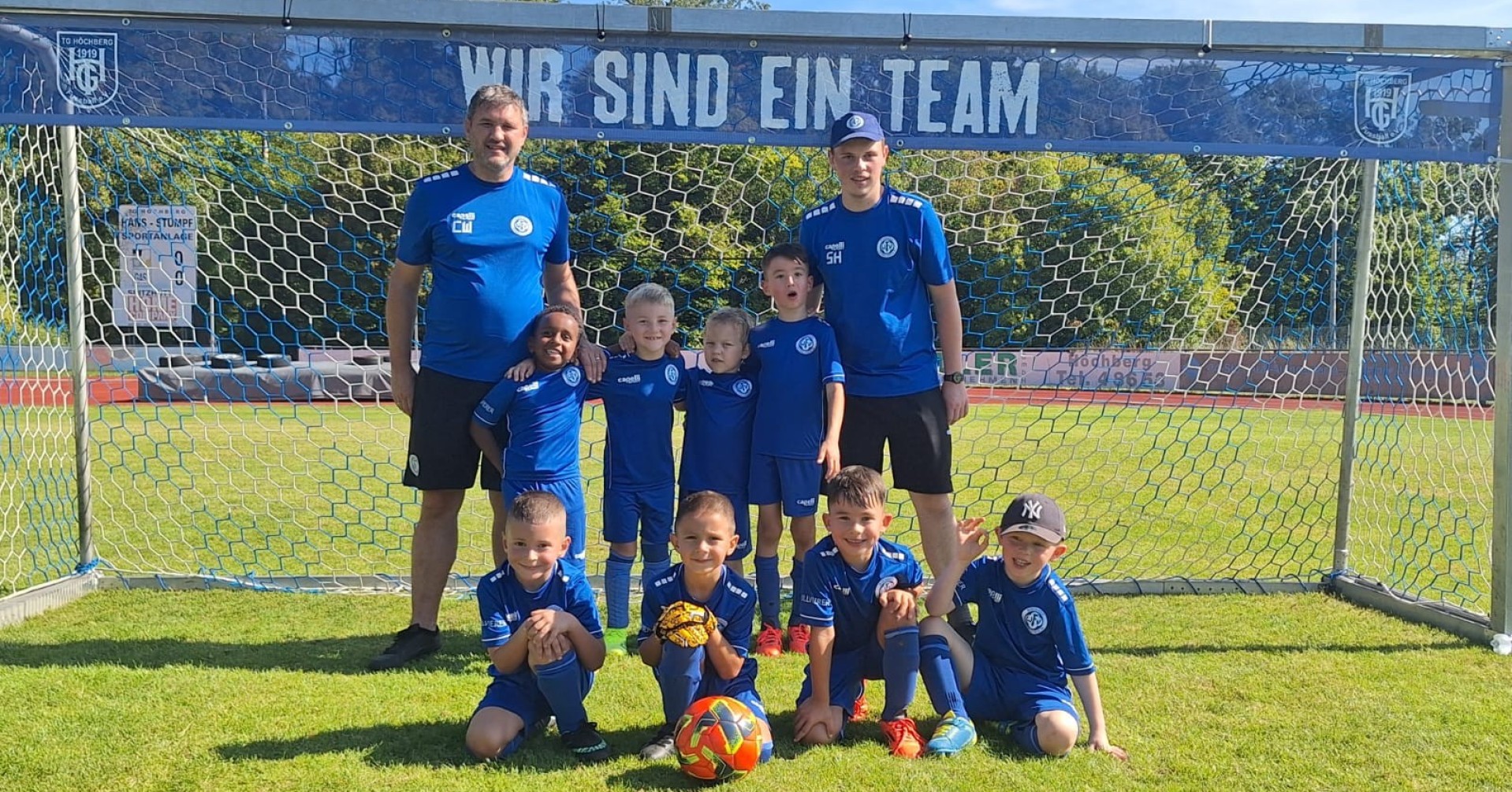 Jugendfußballmannschaft mit Trainern vor einem Tor mit dem Schriftzug 'Wir sind ein Team'