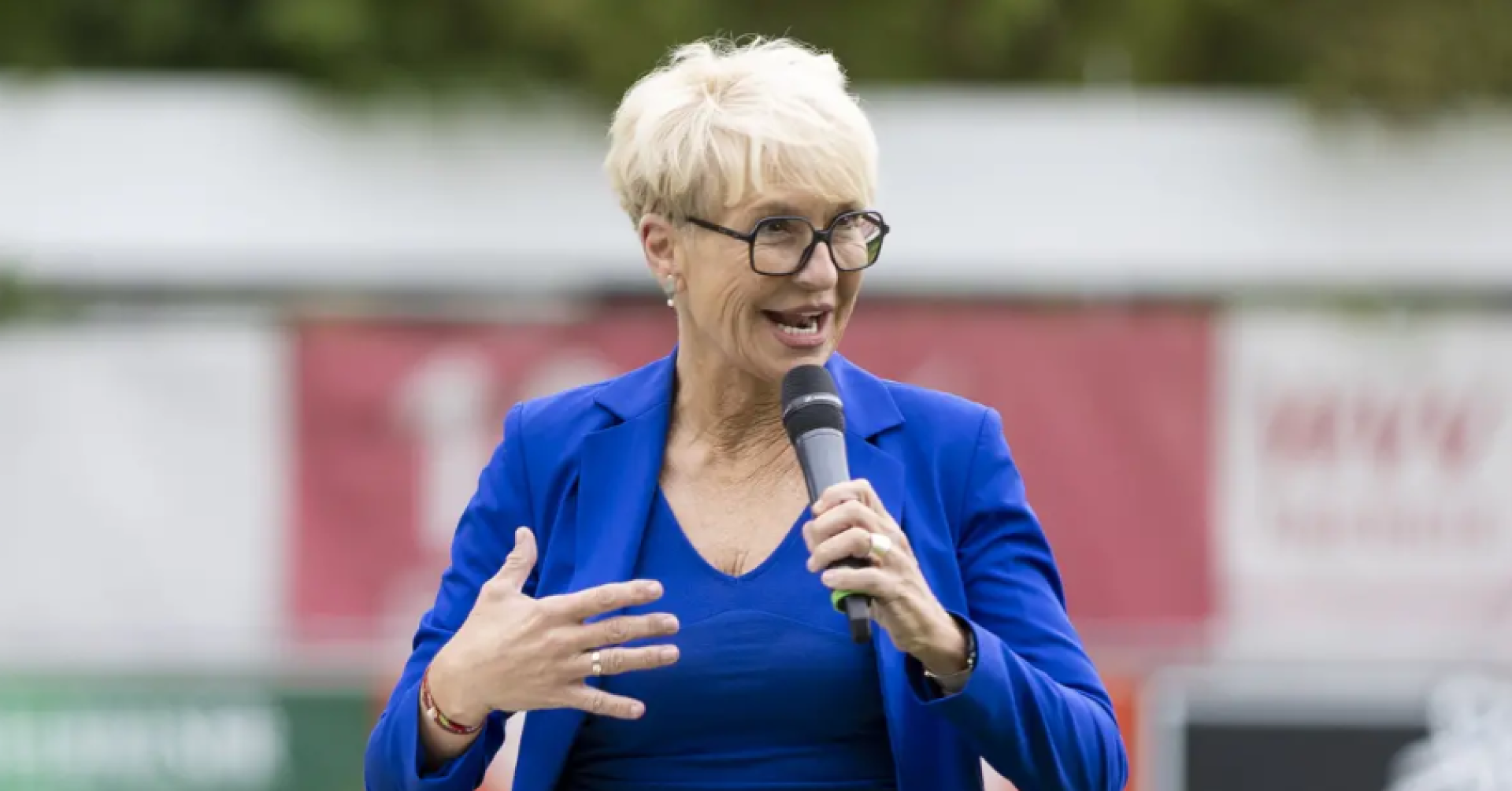 Frau im blauen Blazer hält ein Mikrofon und spricht bei einer Veranstaltung im Freien